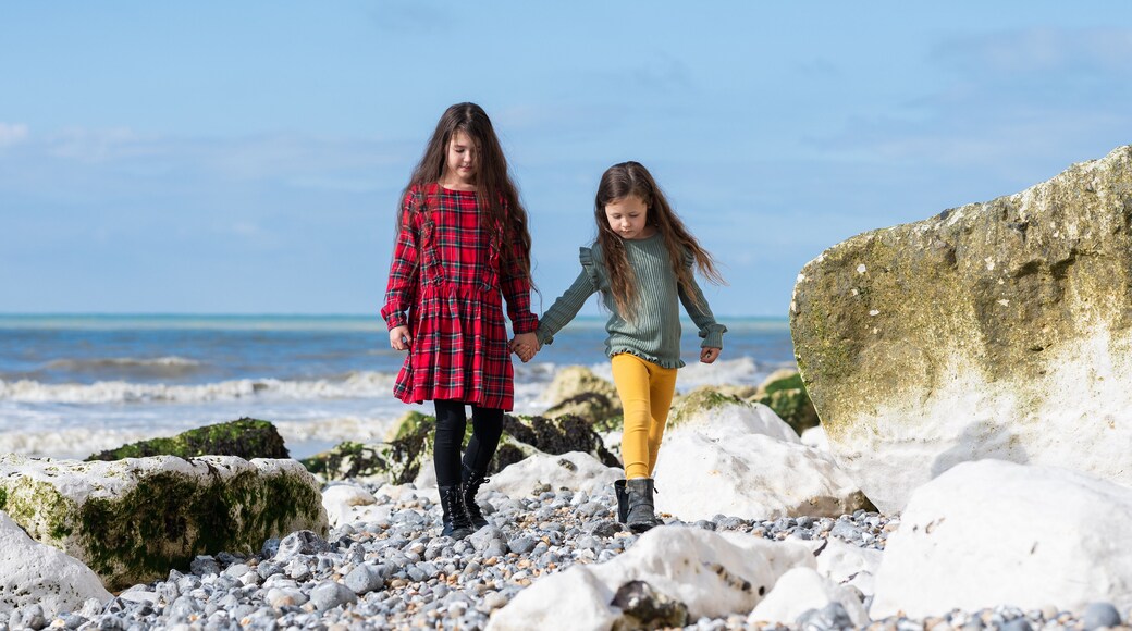Two little girls in red tartan dress, green jumper and yellow leggings walking at Hope Gap beach near Cuckmere Haven located between Seaford and Eastbourne in East Sussex, British south coast