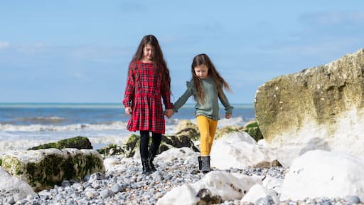 Two little girls in red tartan dress, green jumper and yellow leggings walking at Hope Gap beach near Cuckmere Haven located between Seaford and Eastbourne in East Sussex, British south coast