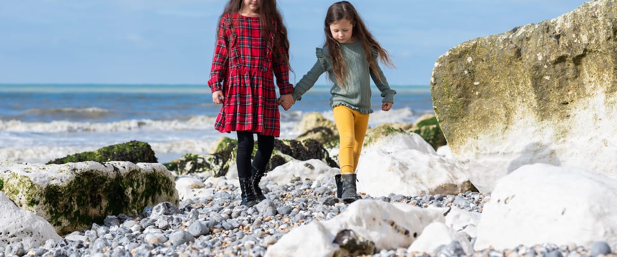 Two people walking on a rocky beach with the ocean in the background.