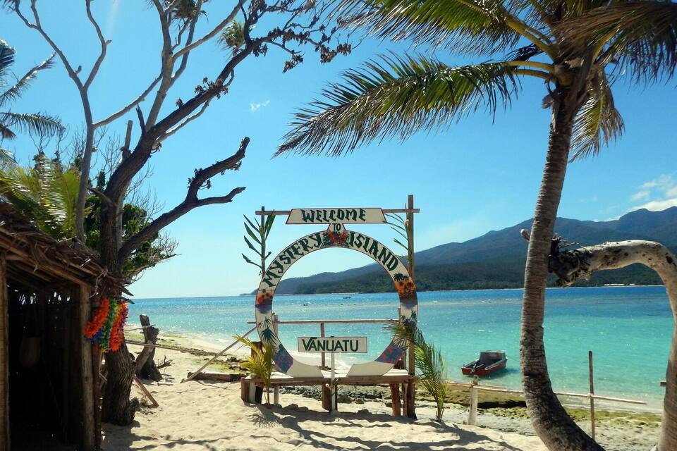 A beach with a 'Welcome to Vanuatu' sign, palm trees, and clear blue water.
