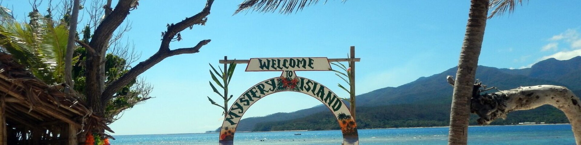 Una playa con un cartel que dice 'Welcome to Vanuatu', palmeras y agua azul cristalina.