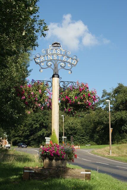 A signpost with 'East Grinstead' written on it, surrounded by flowers and greenery.