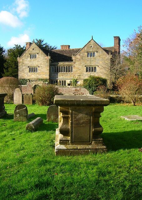 A stone building with a grassy lawn and gravestones in the foreground.
