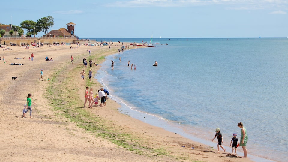 A sandy beach with people walking and swimming, a lifeguard tower, and boats in the water.