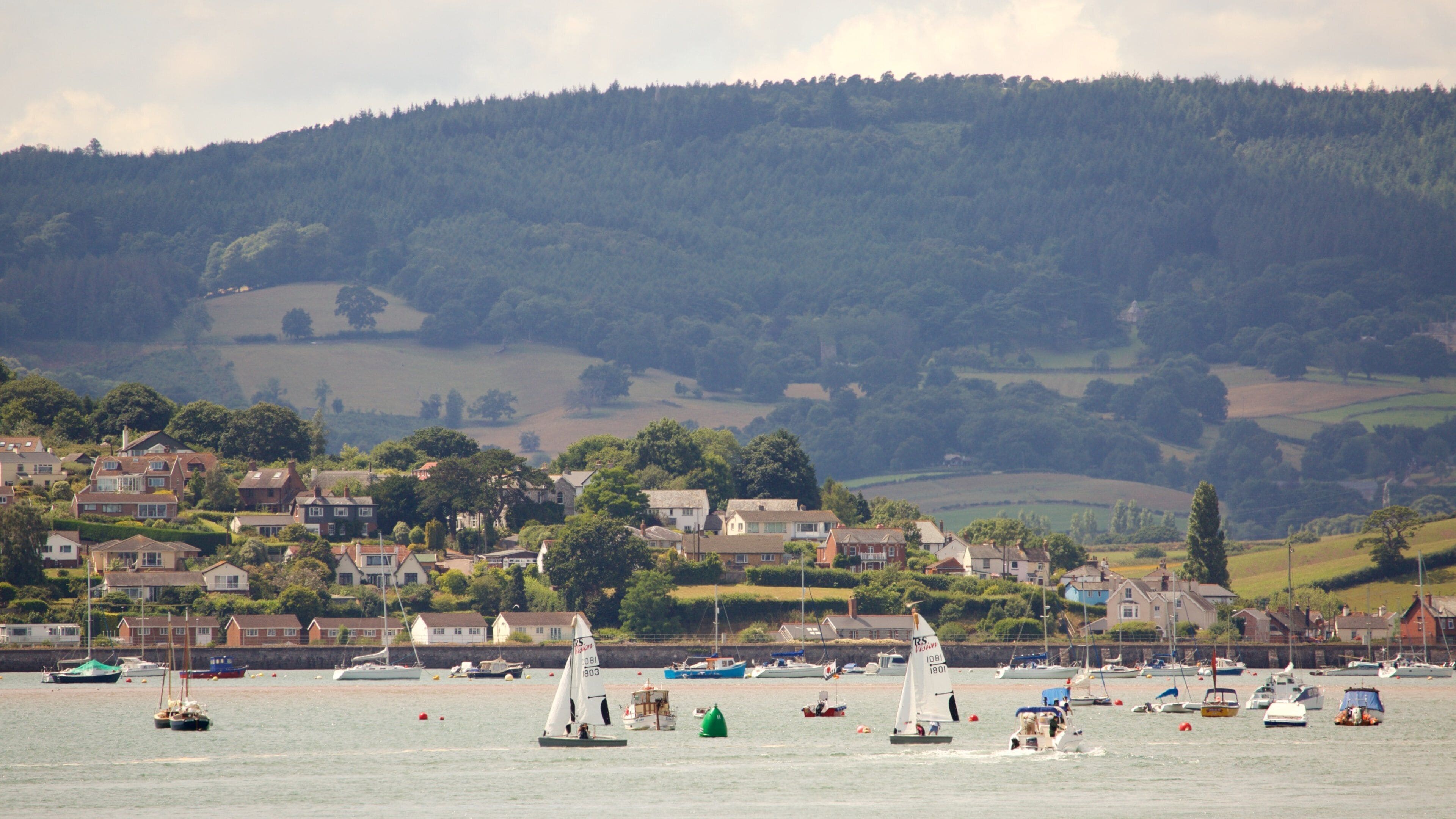A coastal town with sailboats on the water, surrounded by houses and hills.