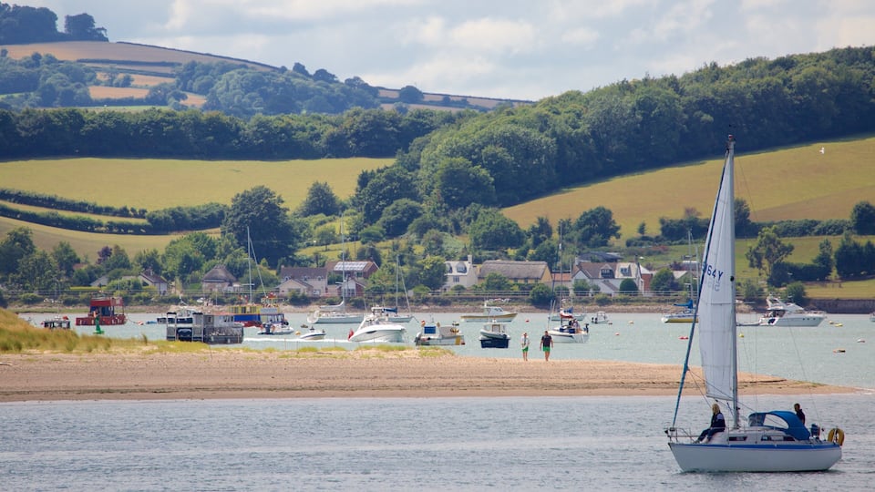 A sailboat on a calm lake with houses and boats in the background.