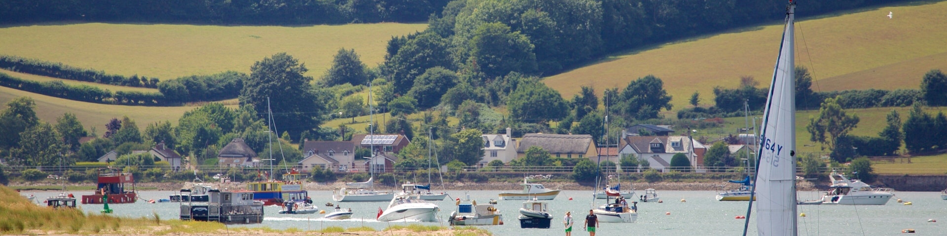 A sailboat on a calm lake with houses and boats in the background.