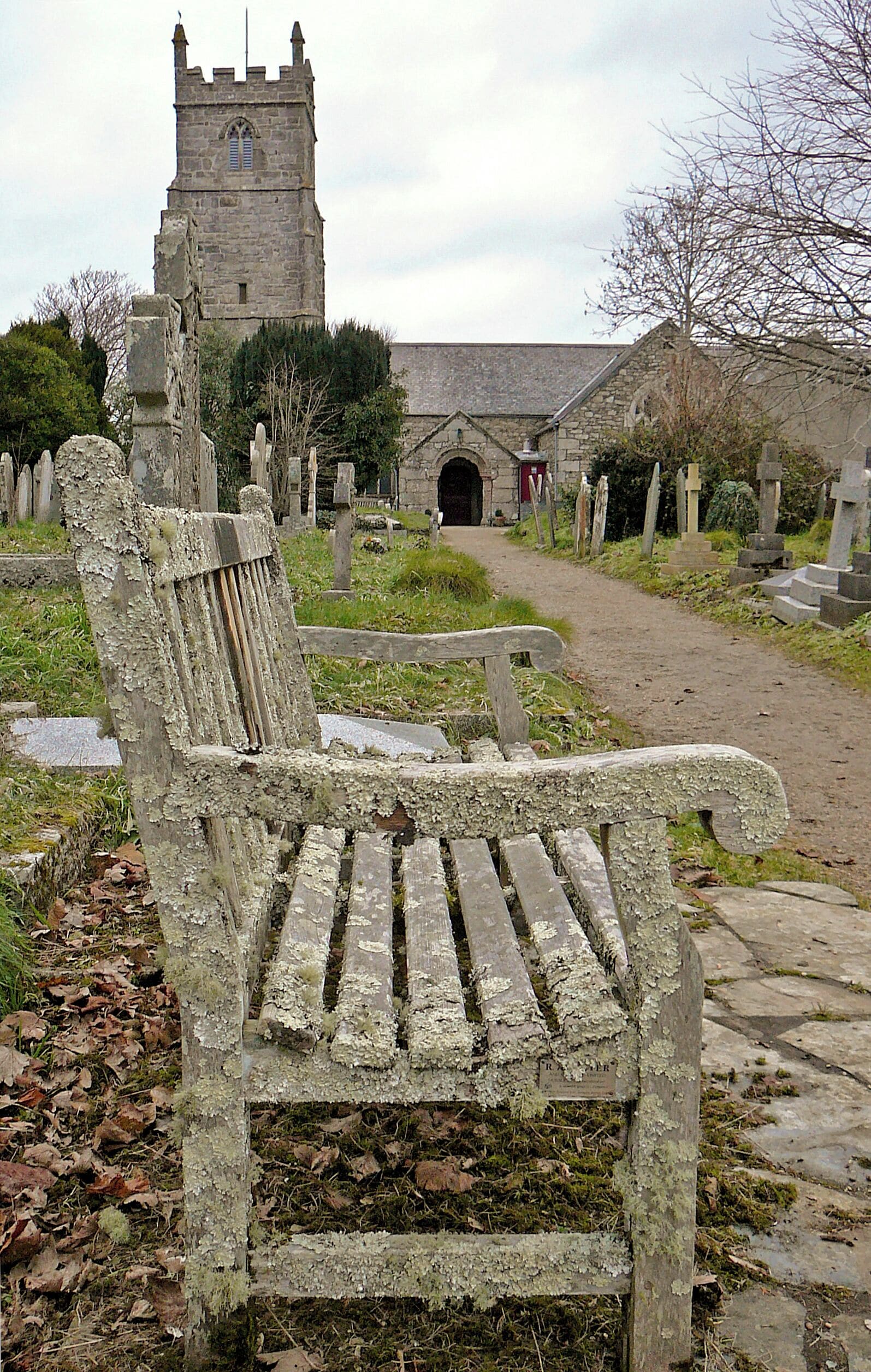 A weathered stone bench in a cemetery with a church tower in the background.
