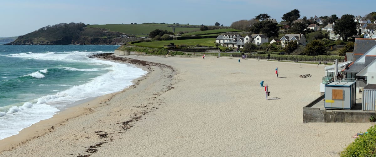 A coastal beach with waves, a sandy shore, and houses in the background.