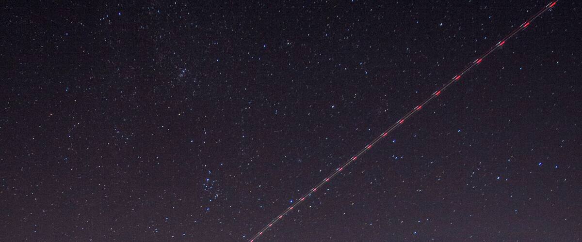 A starry night sky over a coastal town with a visible contrail.