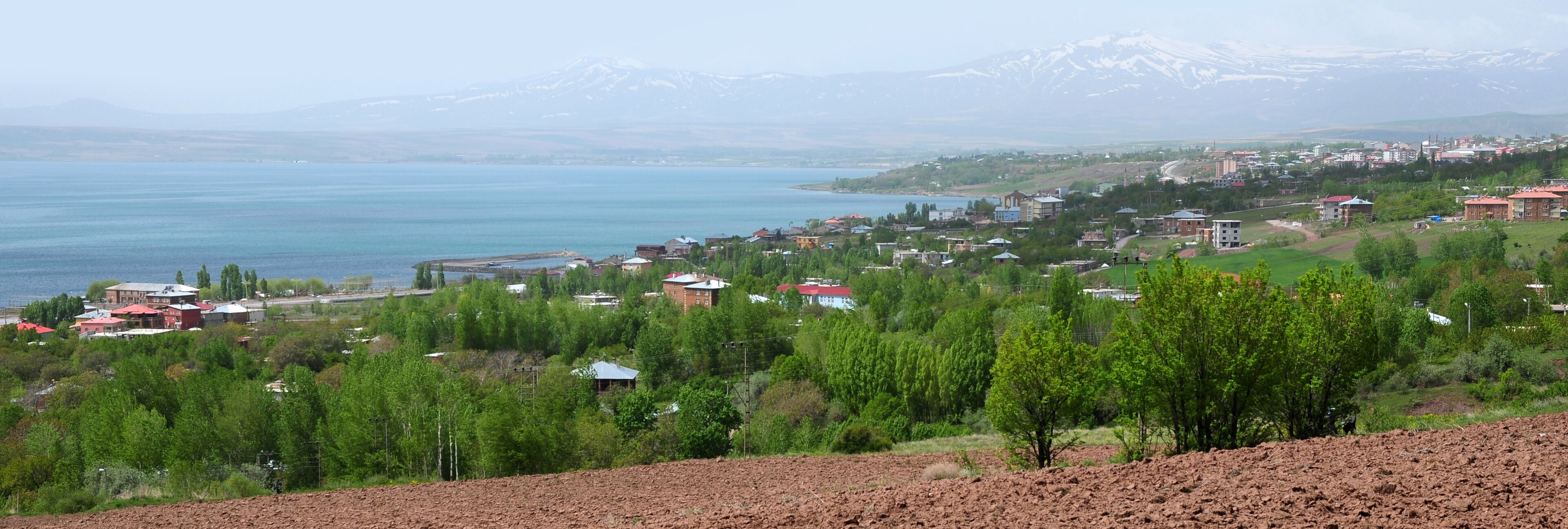 A coastal town with a lake, green hills, and snow-capped mountains in the background.