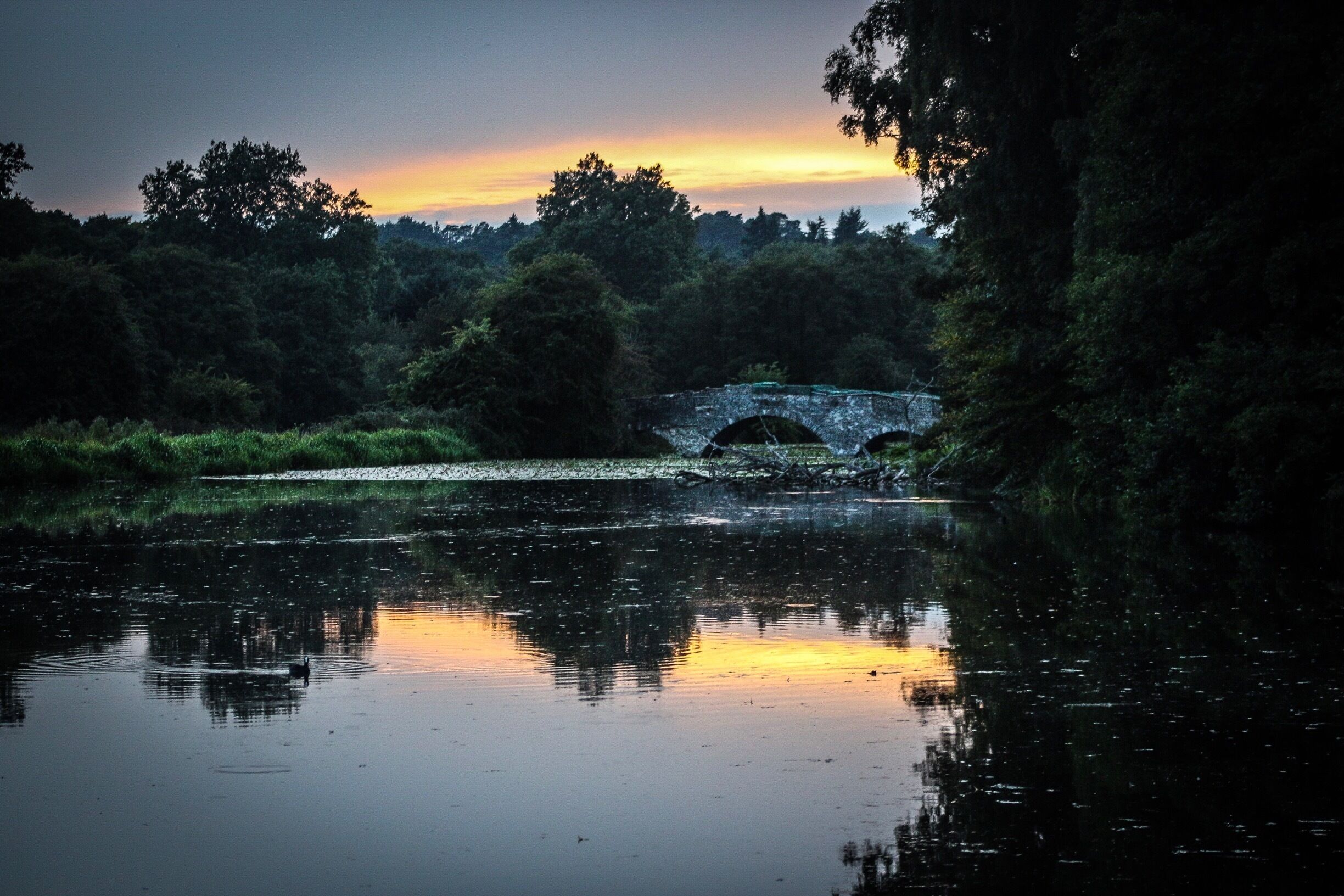 Uma ponte de pedra sobre um rio calmo ao pôr do sol.