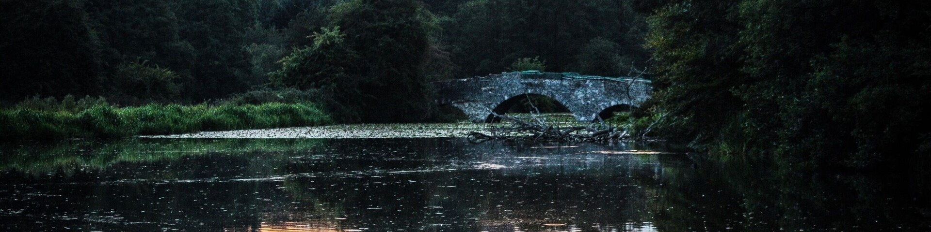 Uma ponte de pedra sobre um rio calmo ao pôr do sol.