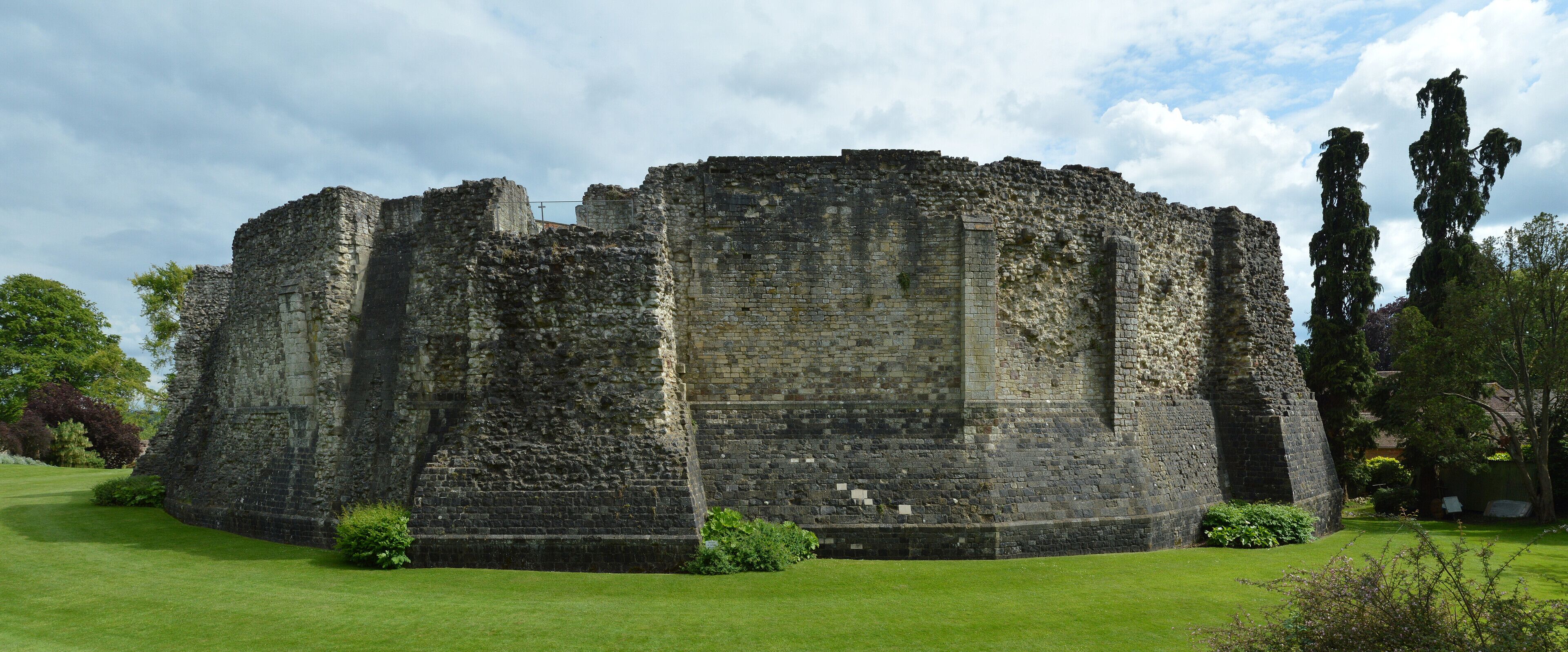 A historic stone castle with a grassy courtyard and tall trees.