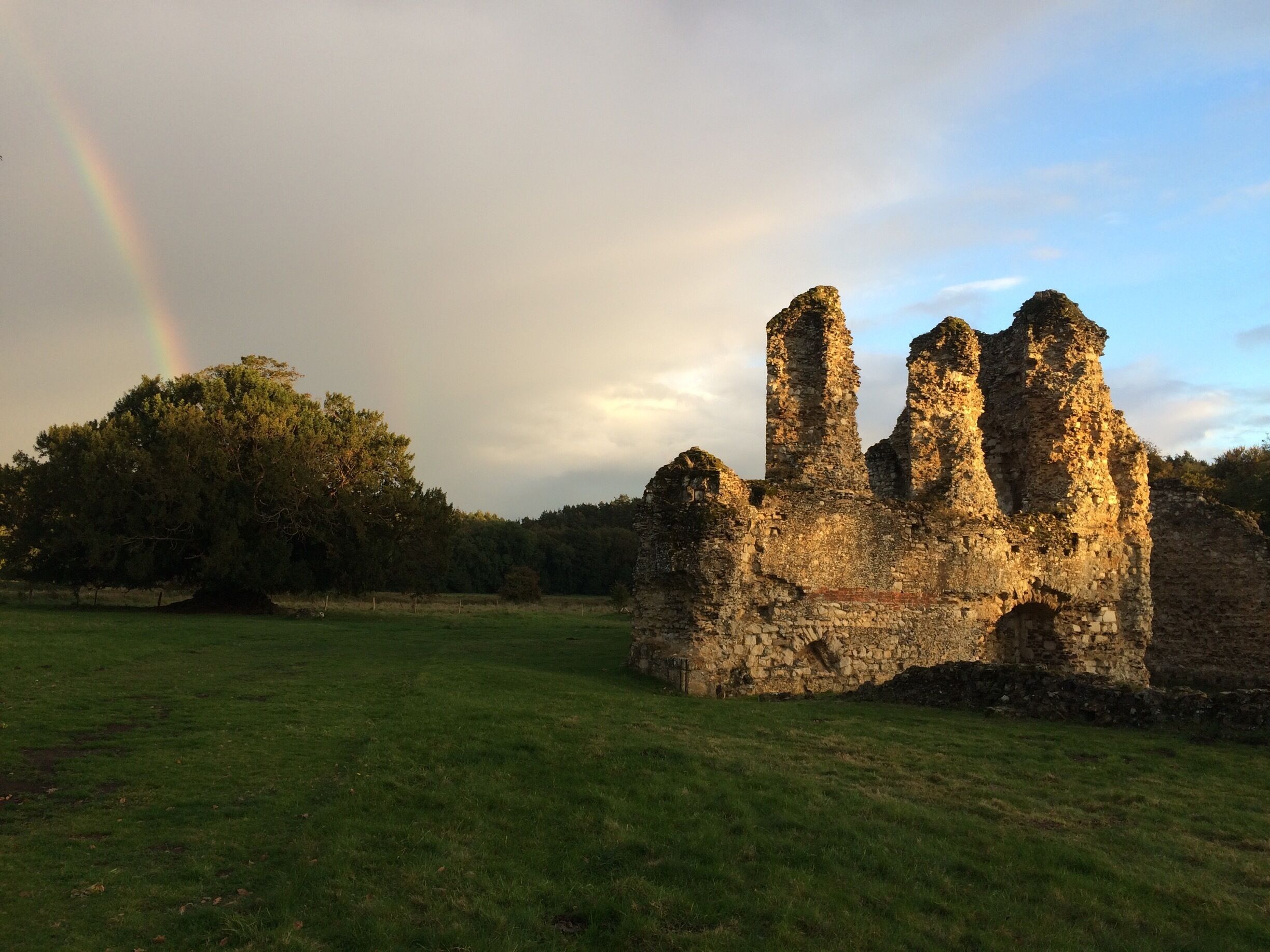 A stone ruin with three towers, a rainbow, and a forest in the background.