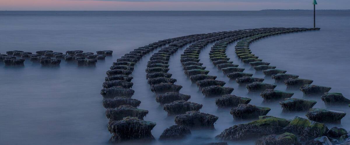 A long, curved breakwater extending into calm waters at sunset.