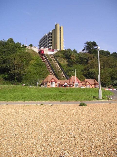 A building with a steep driveway, a gravel area, and a red-roofed structure.