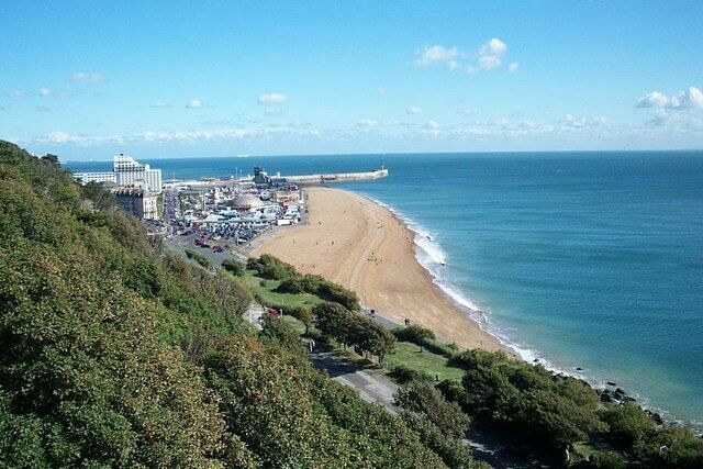 A coastal landscape with a beach, ocean, and a building complex on a hillside.