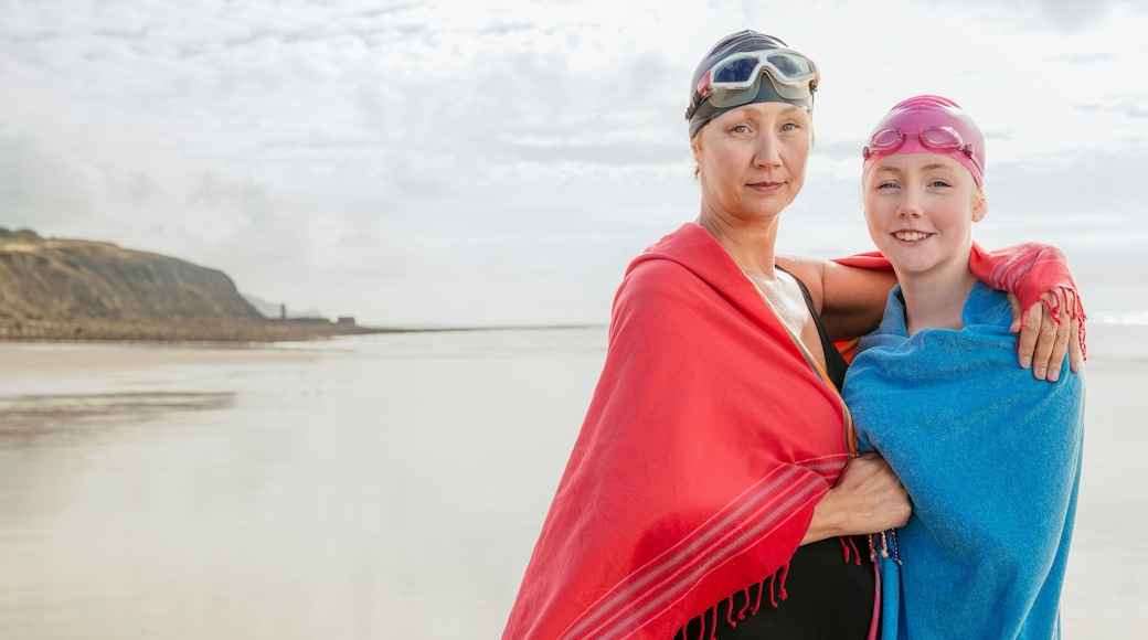 Mother and daughter standing on beach with shawls, Folkestone, UK