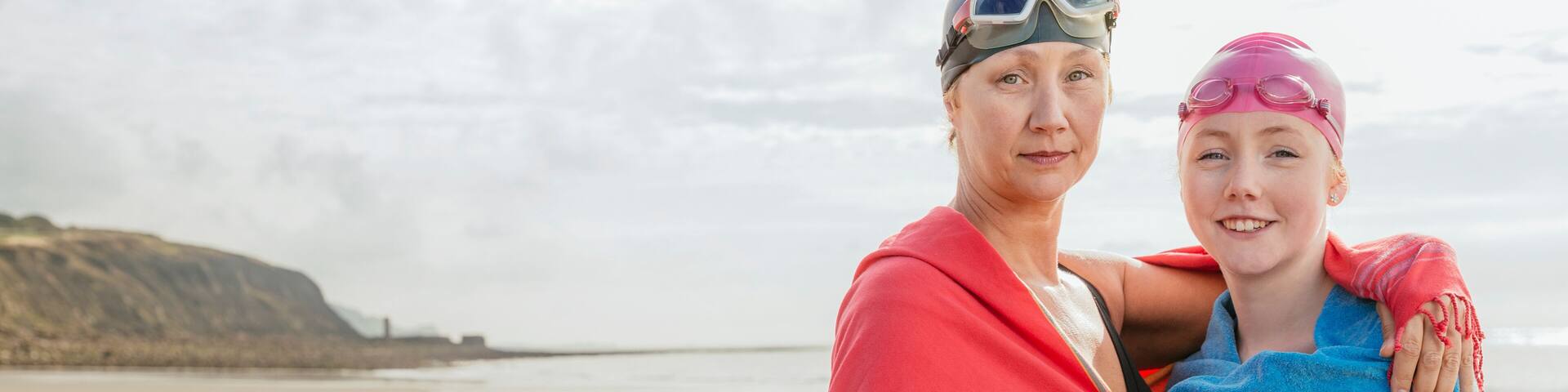 Mother and daughter standing on beach with shawls, Folkestone, UK