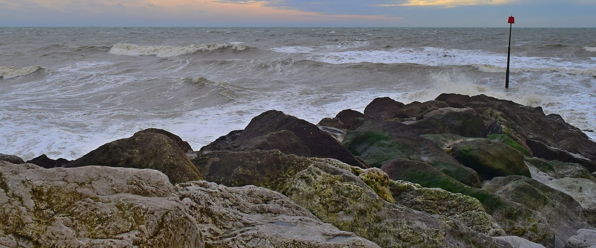 A rocky shoreline with waves crashing against the rocks and a red buoy in the water.