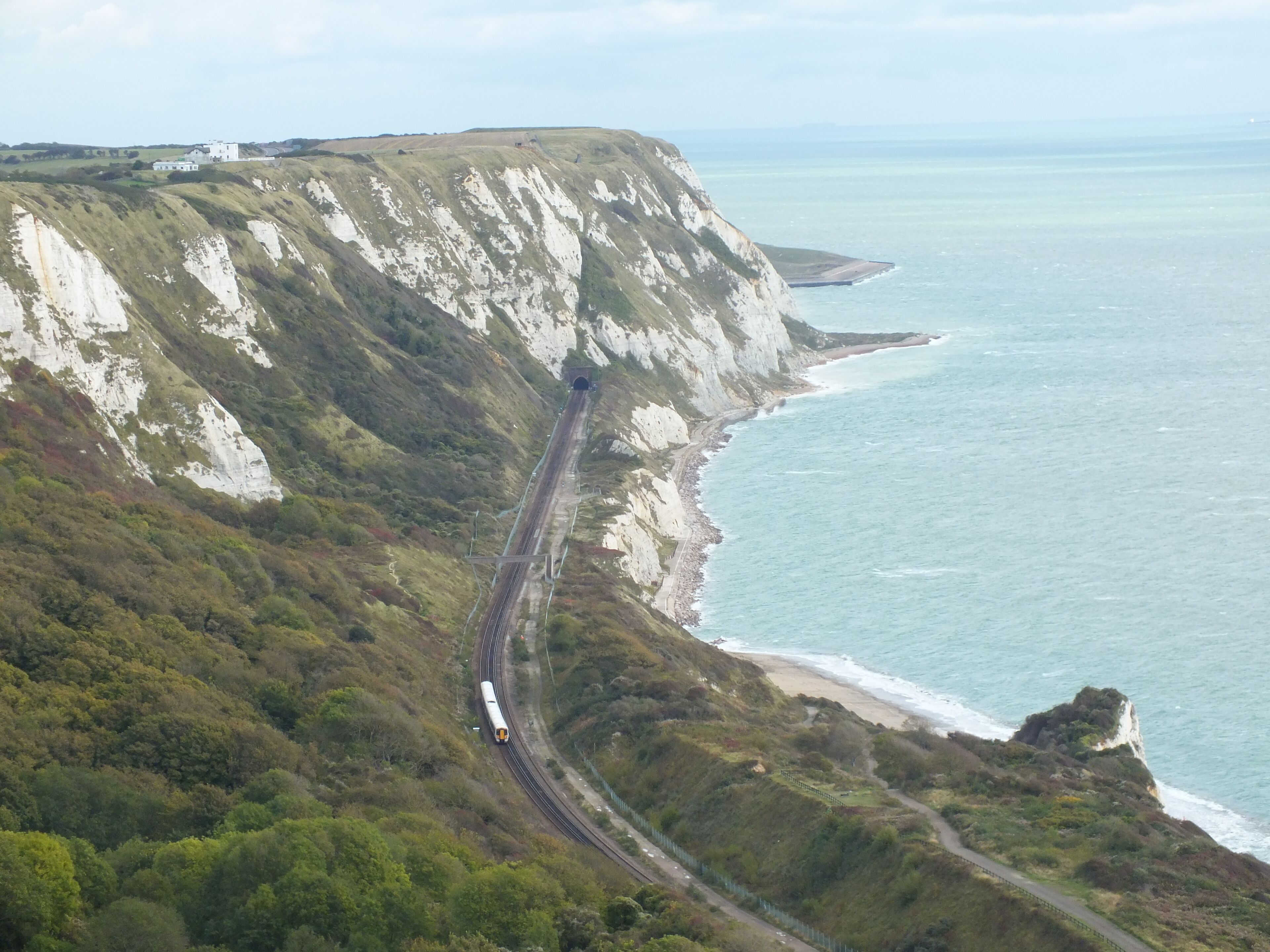 A coastal railway track curving along a cliffside with a beach and ocean in the background.