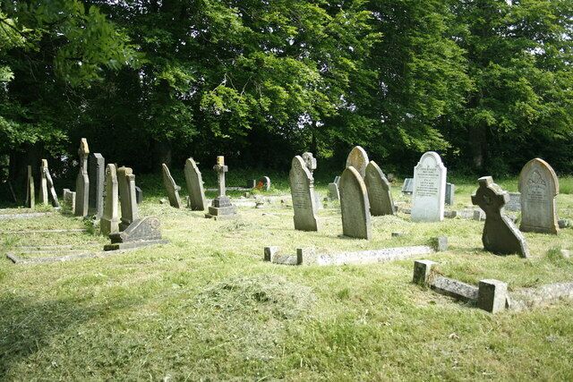 A cemetery with numerous headstones and crosses, surrounded by trees.