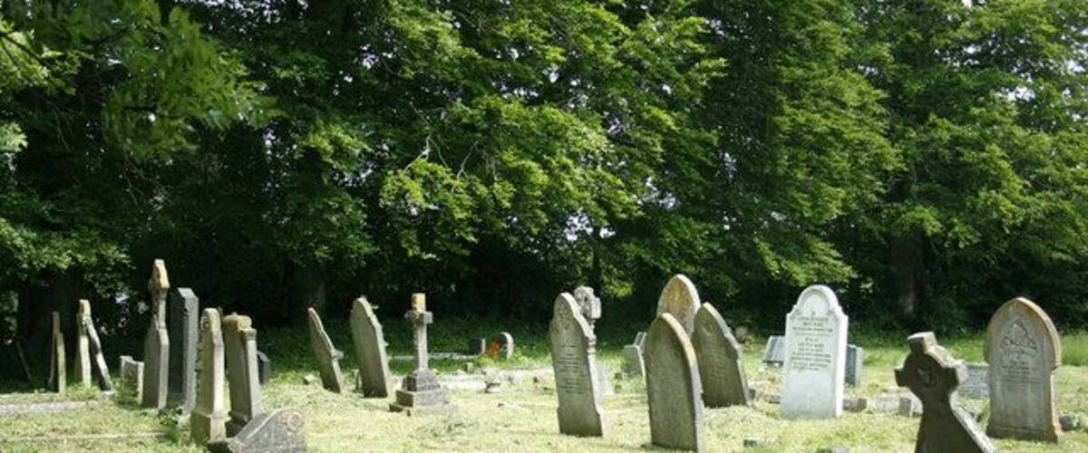 A cemetery with numerous headstones and crosses, surrounded by trees.