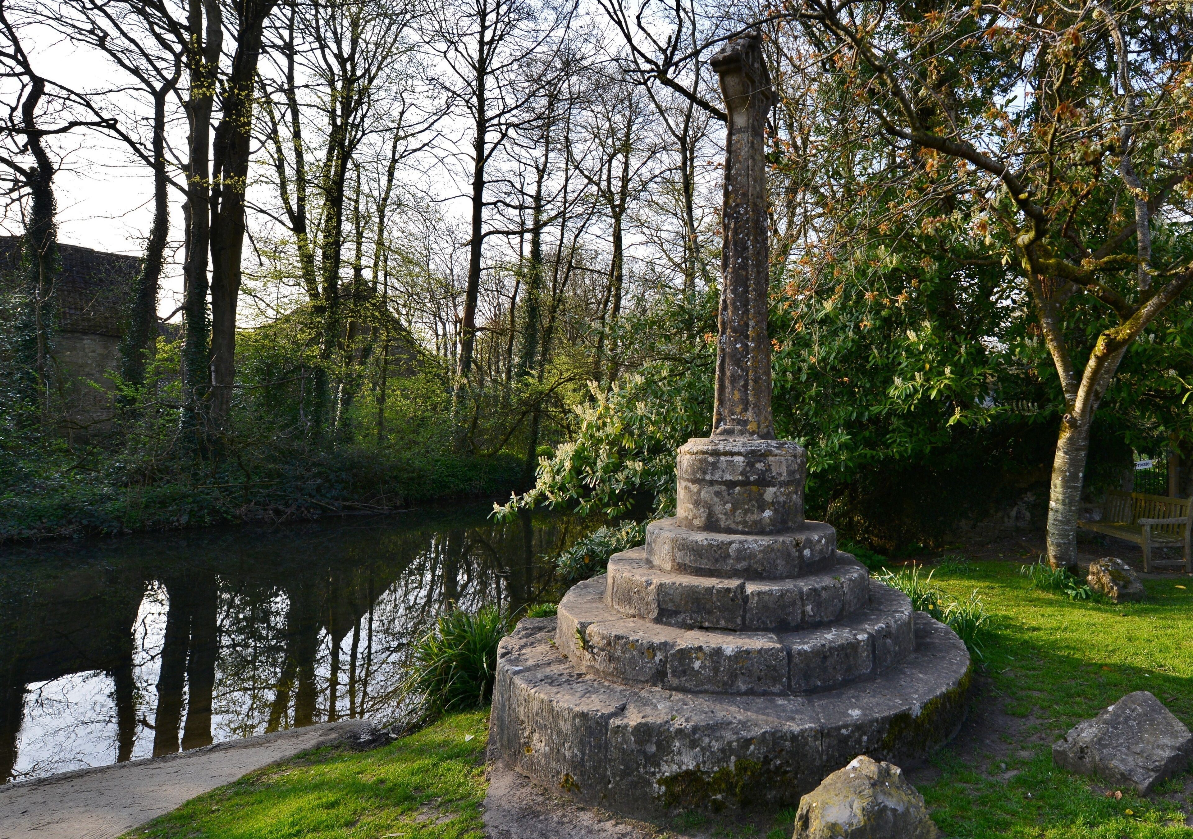 A stone monument by a calm river, surrounded by trees and grass.