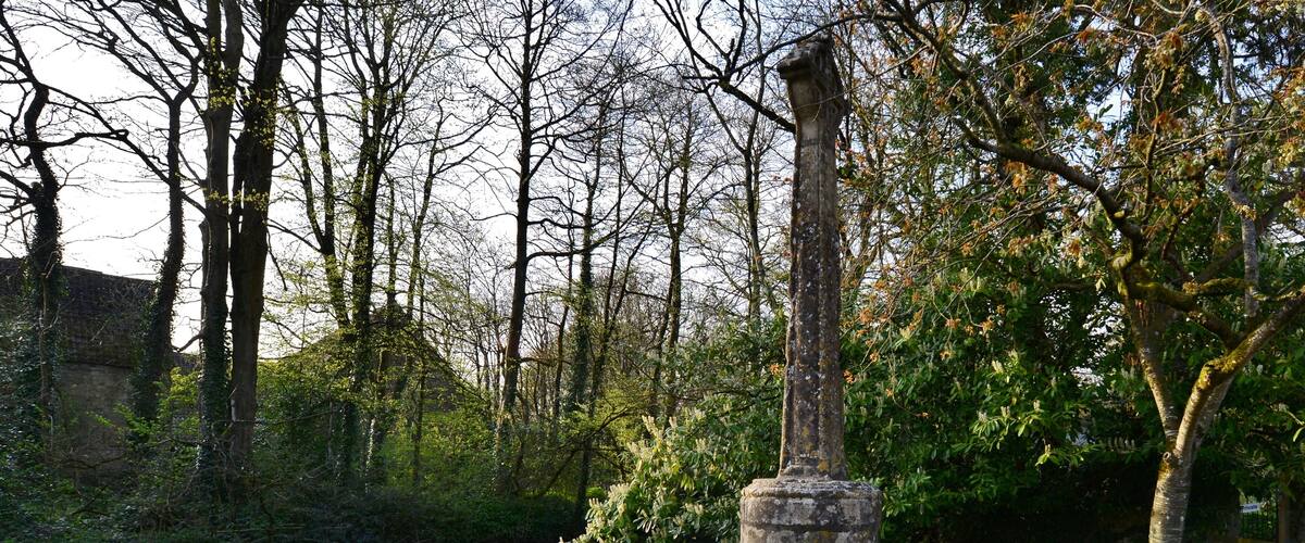 A stone monument by a calm river, surrounded by trees and grass.