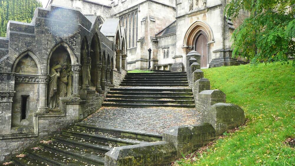 Eine historische Steintreppe, die zu einem Gebäude mit Rundbogenportalen und Statuen führt.