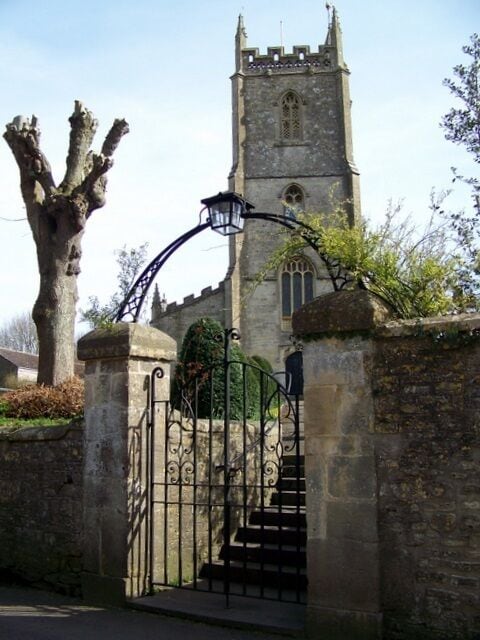 Un portón de piedra que da acceso a una iglesia con una alta torre y una entrada abovedada.