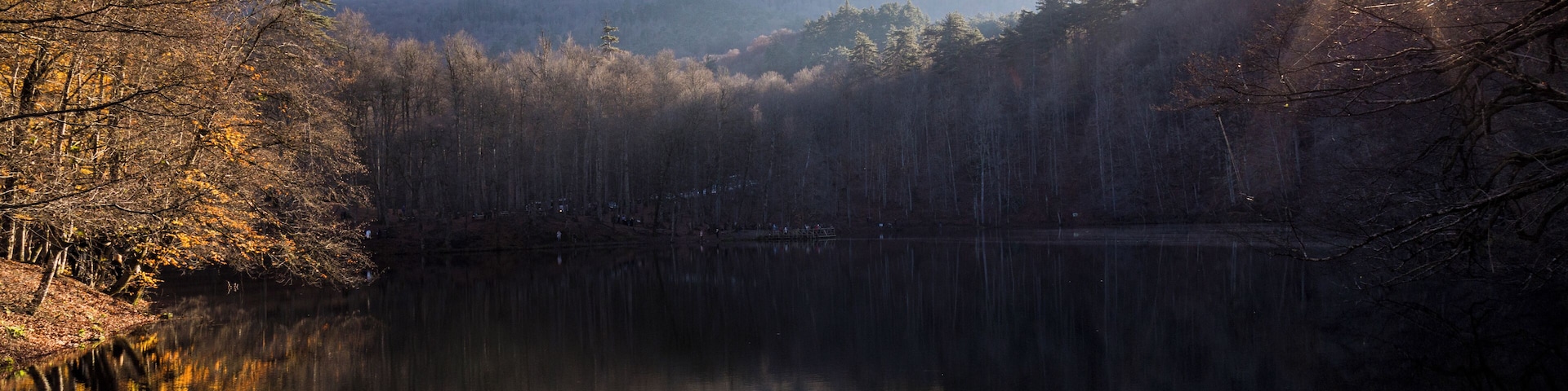 A calm lake surrounded by autumn trees and a misty mountain in the background.