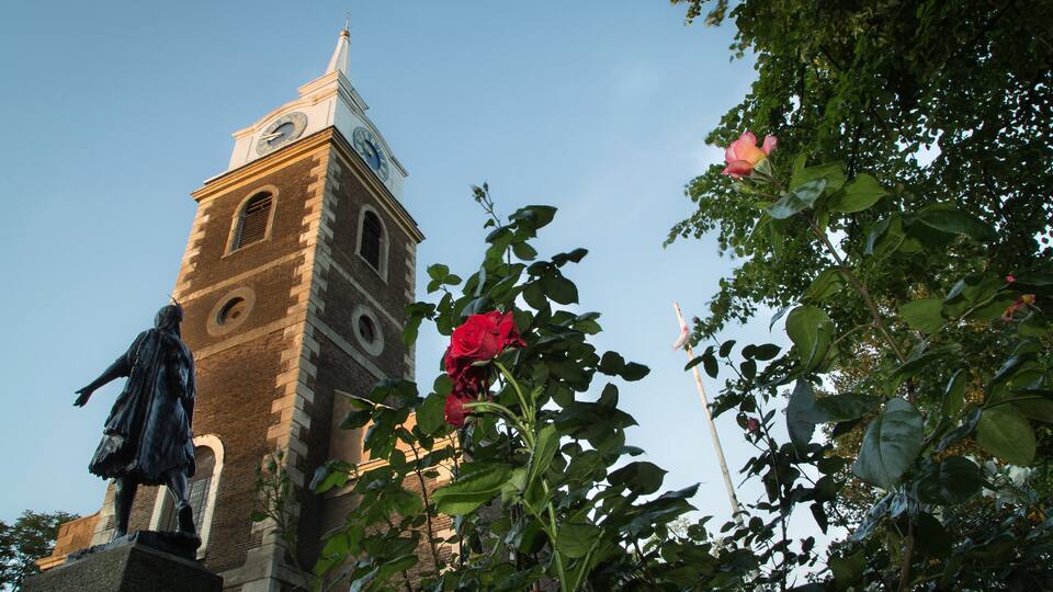 A clock tower, a statue, and a rose bush.