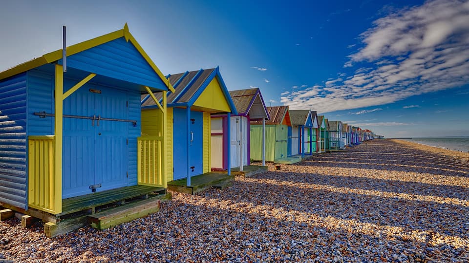 A row of colorful beach huts on a pebbled beach.