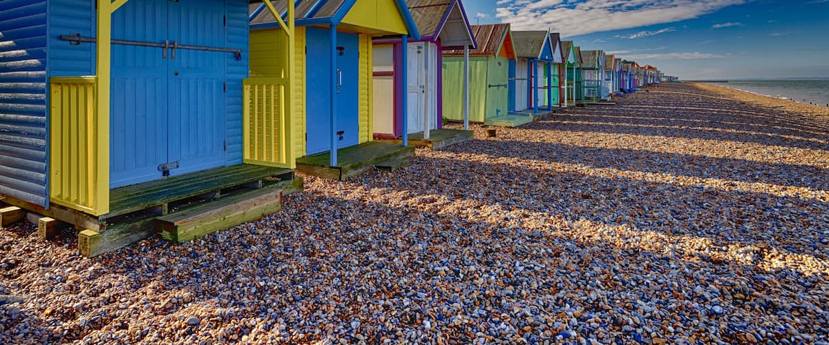 A row of colorful beach huts on a pebbled beach.