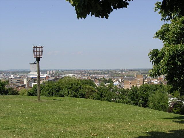 A grassy hill with a street lamp, a cityscape in the background, and trees.