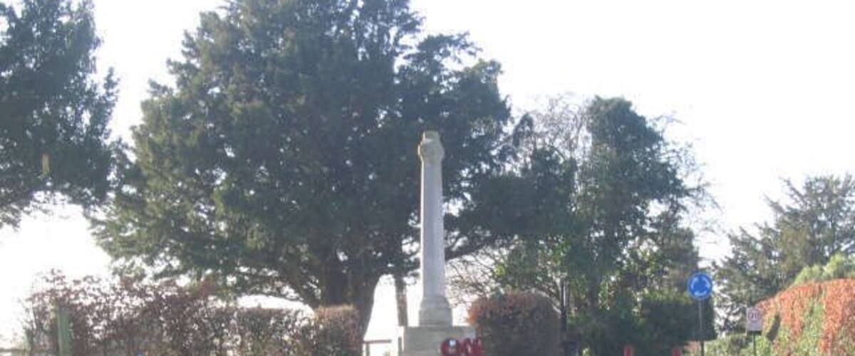 A memorial with a tall obelisk, white headstones, and a road with a blue circular sign.