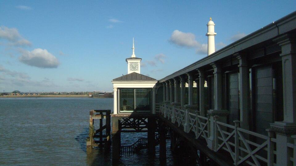 A pier extending over water with a clock tower and a lighthouse in the background.