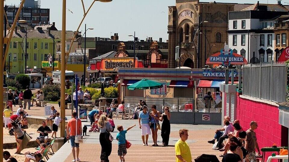 A busy promenade with people walking, a family diner, and a prominent clock tower.
