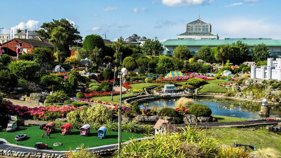 A landscaped garden with a pond, miniature train, and colorful flowers.