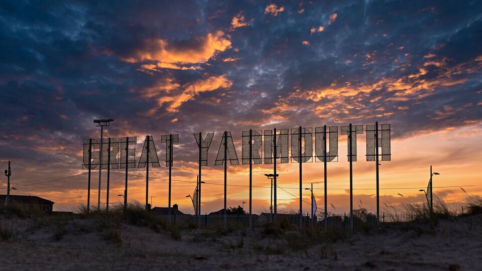 A sunset with clouds and a sign spelling 'GREAT YARMOUTH.'