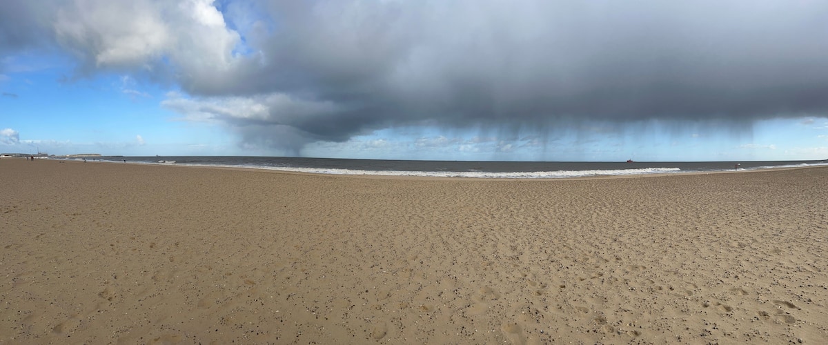 A wide sandy beach with footprints, a calm sea, and a stormy sky.