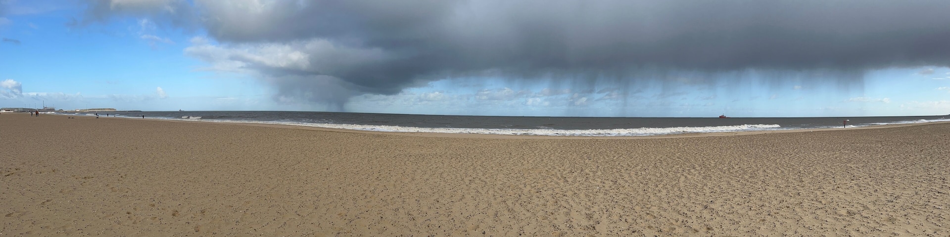 A wide sandy beach with footprints, a calm sea, and a stormy sky.