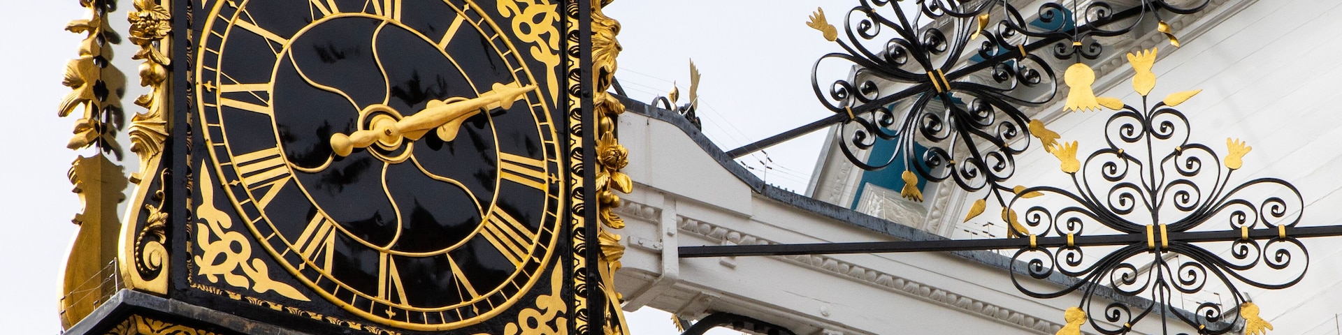 Un reloj grande y ornamentado con números romanos, adosado a un edificio con detalles metálicos decorativos.