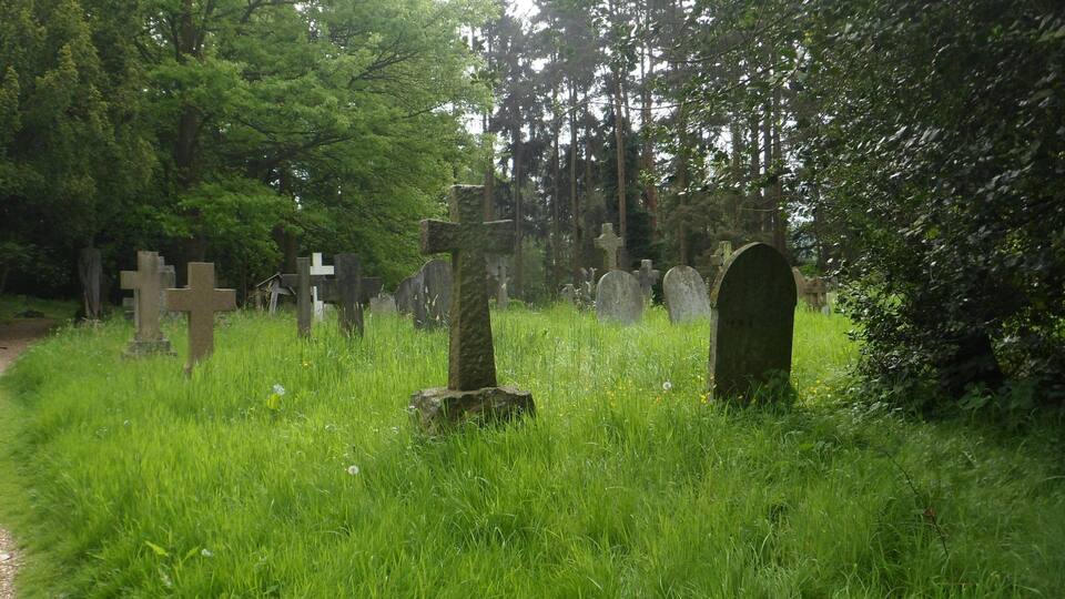 A cemetery with various stone crosses and headstones surrounded by lush greenery and trees.