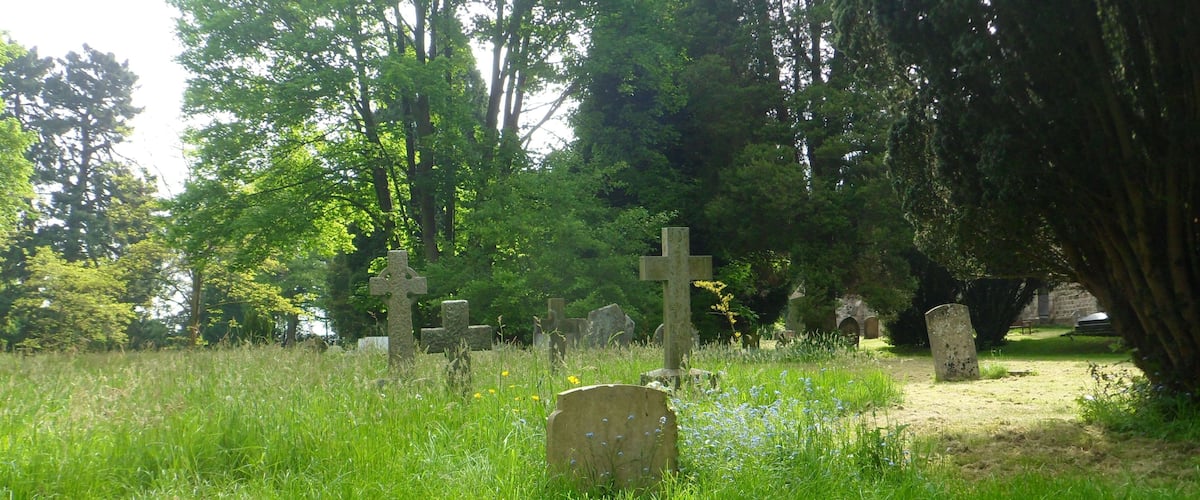 A cemetery with stone crosses and headstones, surrounded by lush greenery and trees.