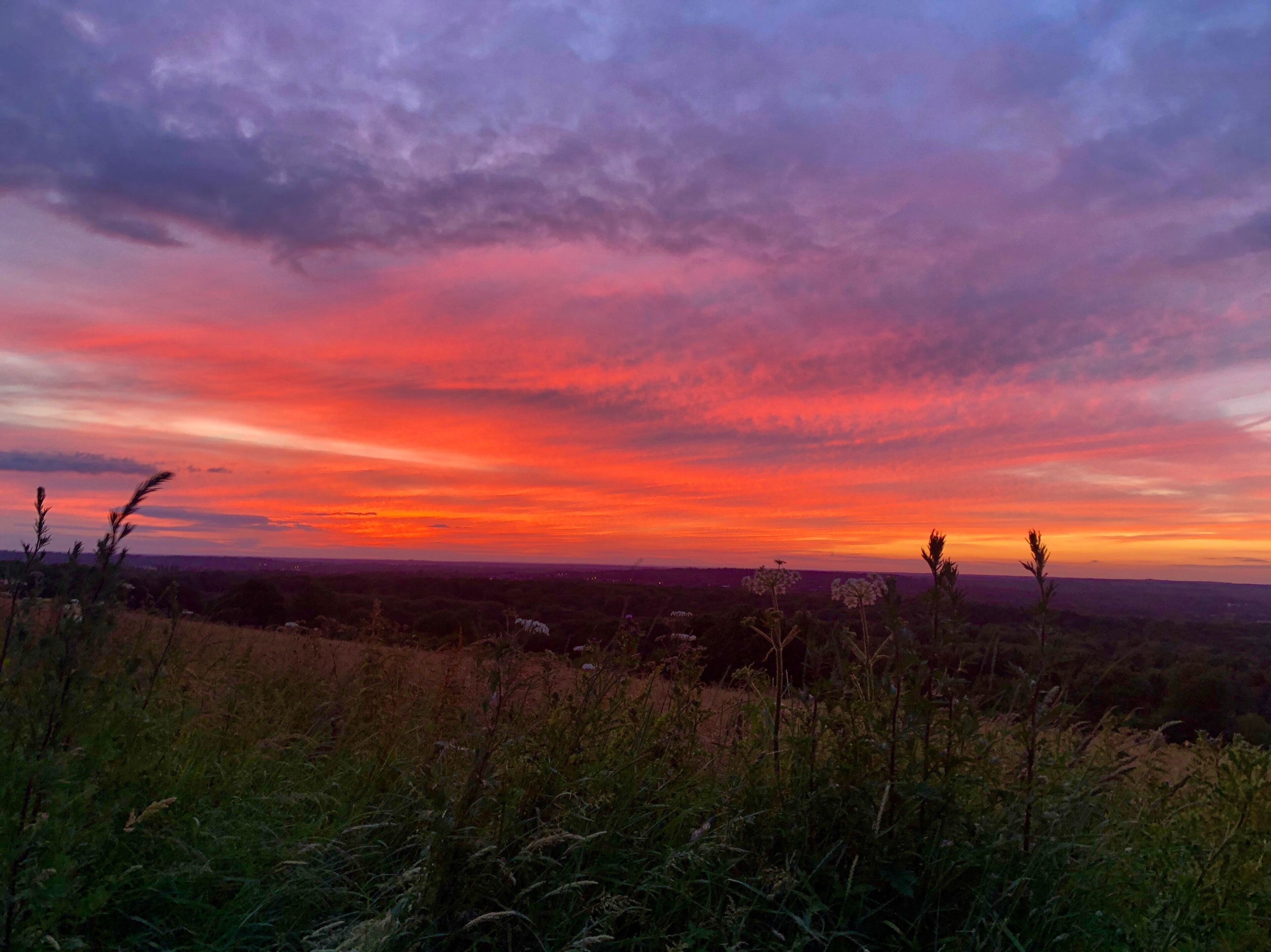 A sunset over a hilly landscape with sparse vegetation and distant city lights.