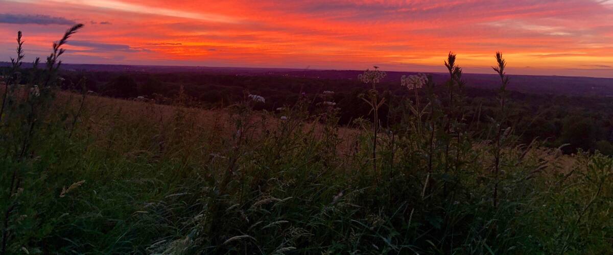 A sunset over a hilly landscape with sparse vegetation and distant city lights.