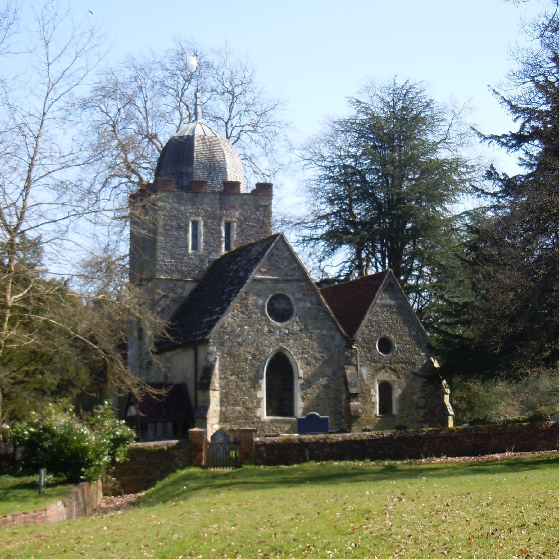 A stone church with a bell tower and a dome, surrounded by trees and a grassy field.